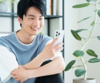 携帯電話を手にして微笑む若い男性、携帯支援のイメージ